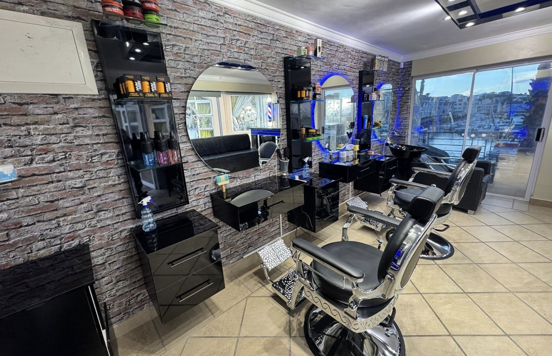 Bay Barber interior: gloss-black stations against exposed brick with round mirrors and blue glow.